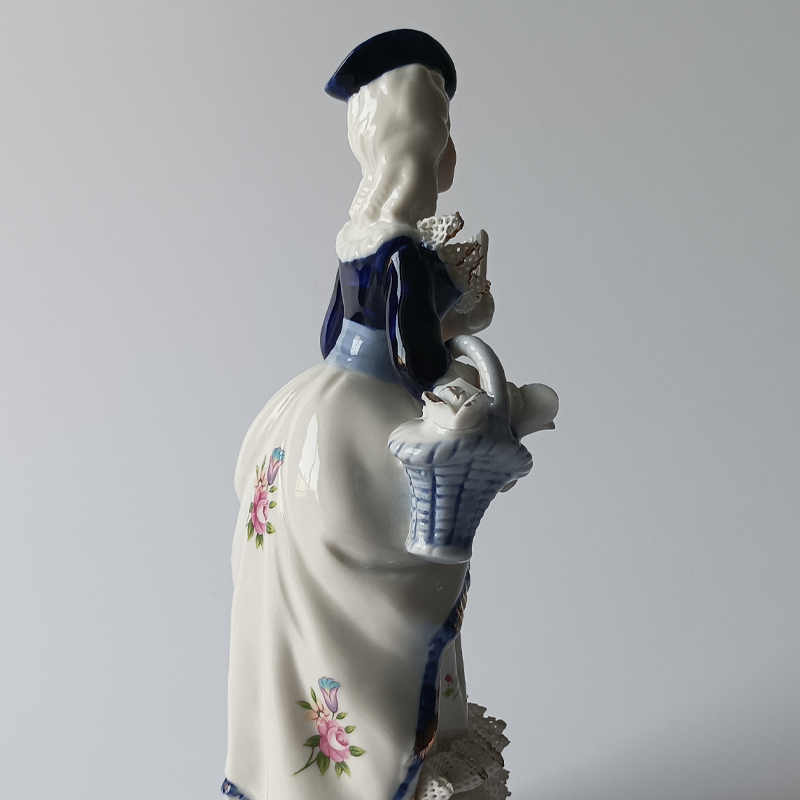 figurka porcelanowa dama dworu Tył porcelanowej figurki, widoczny kapelusz i fałdy sukni.