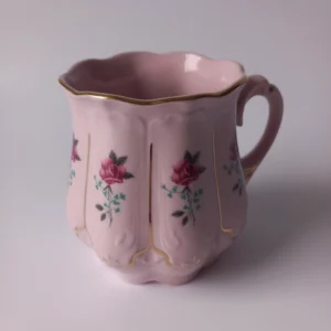 Pękaty kubek z różowej porcelany ze złotym uchem i reliefami.