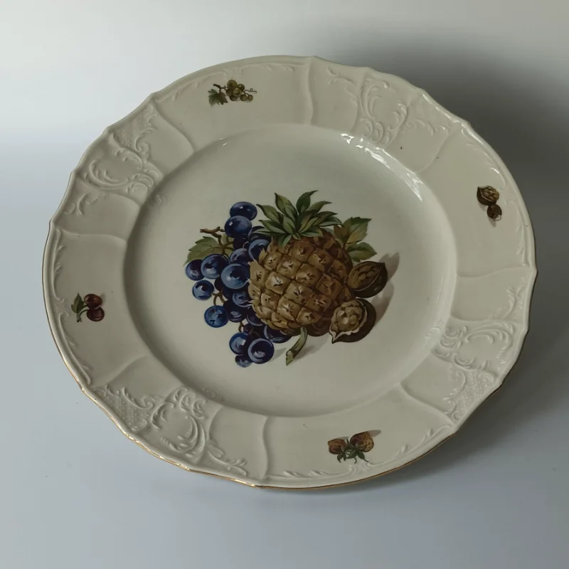 Duży porcelanowy talerz stołowy marki Bernadotte z motywem ananasa i winogron, widok z góry. Duży porcelanowy talerz stołowy marki Bernadotte z motywem ananasa i winogron, widok z góry.