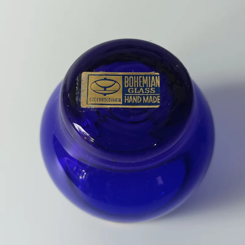 Zestaw sześciu kobaltowych kieliszków ze złotym rantem, ustawionych obok siebie na białym tle. Oryginalna złoto-niebieska naklejka producenta Bohemian Glass Handmade Czechoslovakia na spodzie kieliszka.