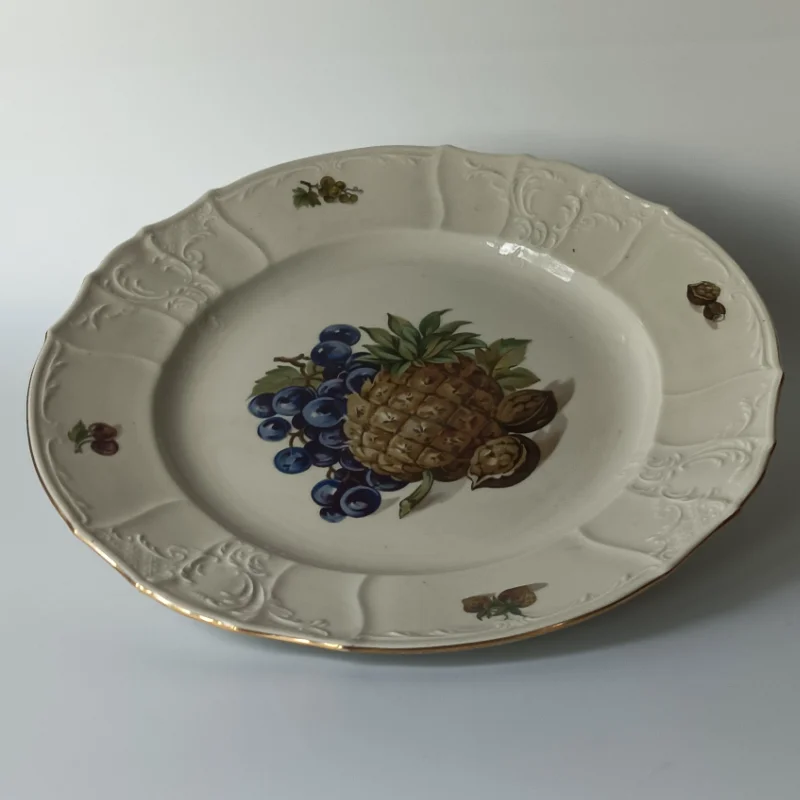 Duży porcelanowy talerz stołowy marki Bernadotte z motywem ananasa i winogron, widok z góry. Porcelanowy półmisek vintage z tłoczonym rantem i delikatnym złoceniem na krawędzi, czeska porcelana.
