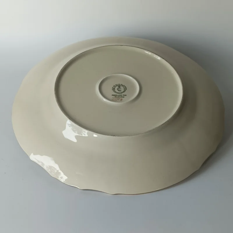 Duży porcelanowy talerz stołowy marki Bernadotte z motywem ananasa i winogron, widok z góry. Spód porcelanowego talerza Bernadotte z widocznym wyprofilowaniem i sygnaturą w centrum.